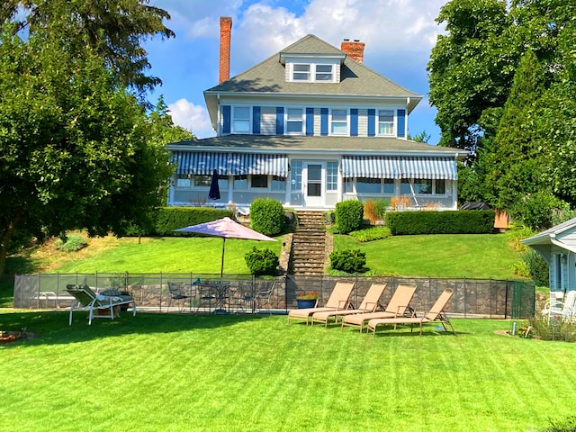 rear view of property with a yard, fence, and a chimney