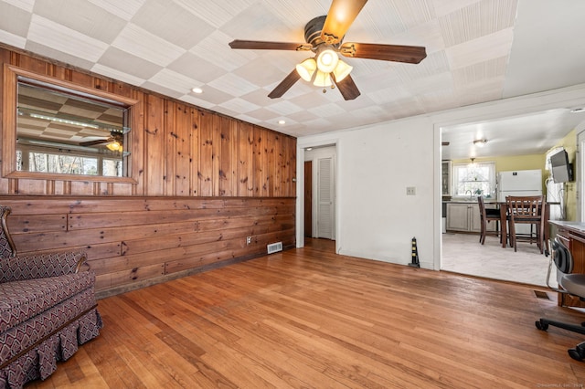 living area with wood walls, a ceiling fan, and light wood finished floors