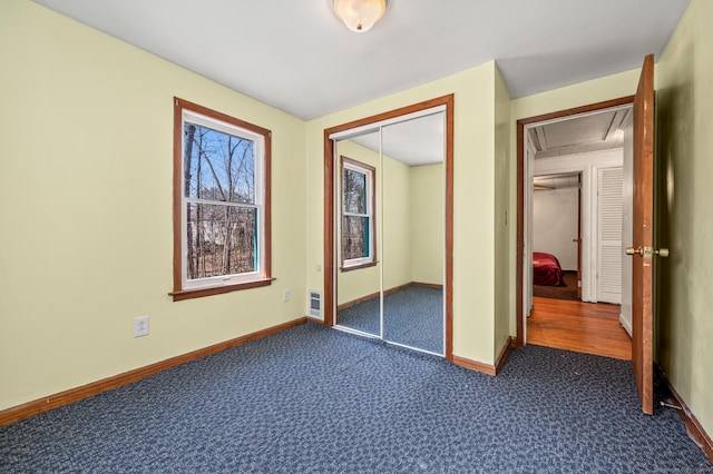 unfurnished bedroom with a closet, dark carpet, attic access, and baseboards