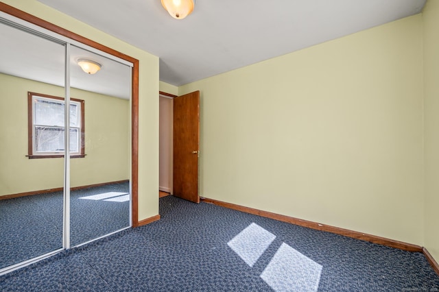 unfurnished bedroom with baseboards, dark colored carpet, and a closet