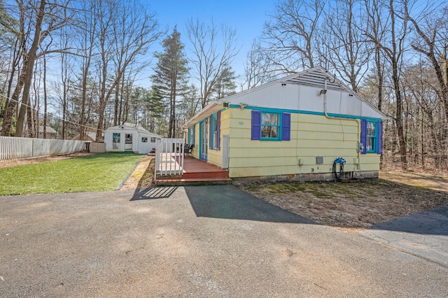 exterior space featuring an outdoor structure, a deck, a front lawn, and fence