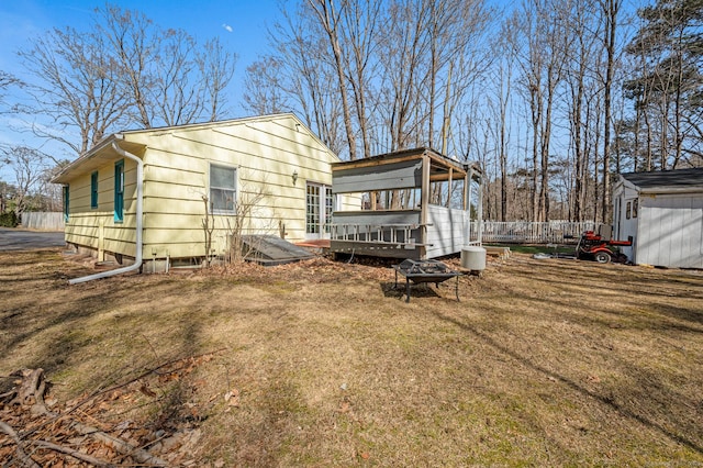 exterior space with an outdoor fire pit, a wooden deck, a lawn, an outbuilding, and a storage unit