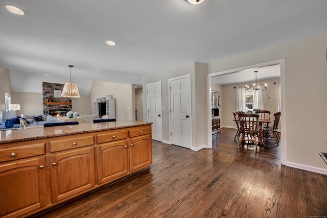 kitchen featuring a notable chandelier, pendant lighting, open floor plan, dark wood finished floors, and a stone fireplace