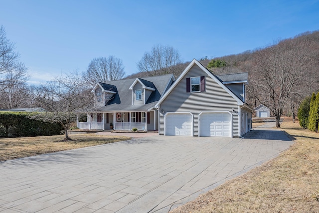 cape cod house with a garage, decorative driveway, and covered porch