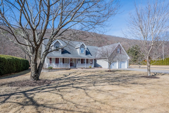 new england style home with covered porch, driveway, and an attached garage