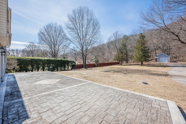 view of patio / terrace with a detached garage, an outdoor structure, driveway, and fence