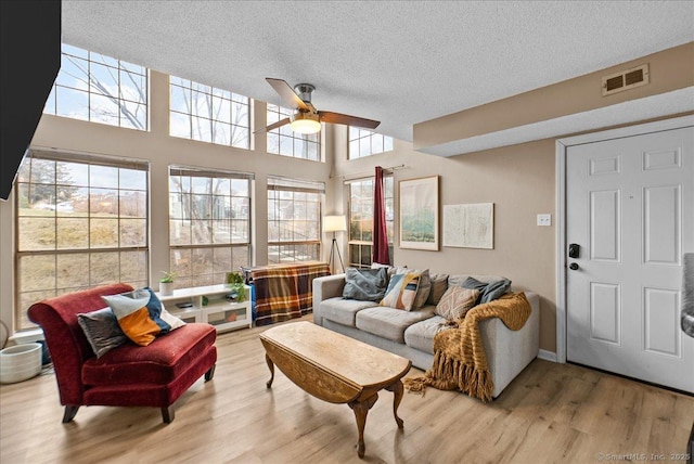 living room featuring visible vents, a ceiling fan, a textured ceiling, wood finished floors, and a towering ceiling