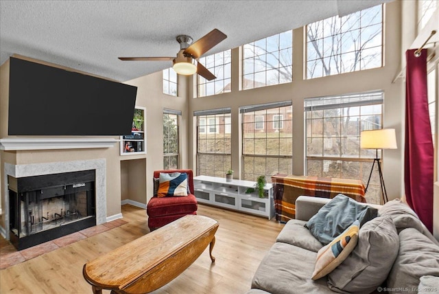 living room with ceiling fan, a fireplace with flush hearth, a textured ceiling, and wood finished floors