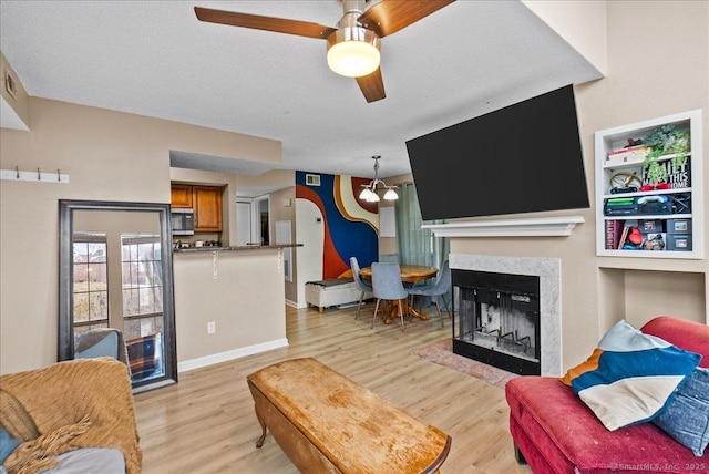 living room featuring light wood finished floors, baseboards, a premium fireplace, a textured ceiling, and a ceiling fan