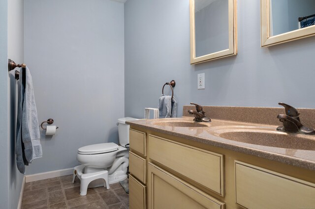 bathroom featuring a sink, baseboards, toilet, and double vanity