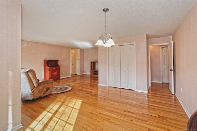 living room with light wood-type flooring, baseboards, a textured ceiling, and an inviting chandelier