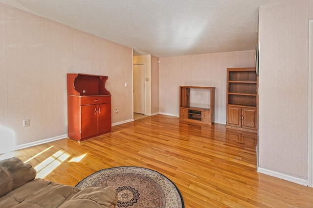 unfurnished living room with baseboards, a textured ceiling, and light wood-style flooring