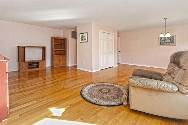 living area featuring wood finished floors, visible vents, baseboards, a textured ceiling, and a notable chandelier