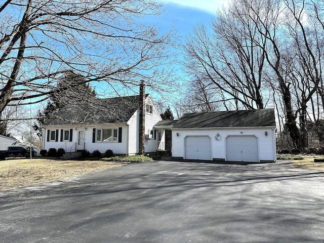 cape cod home with driveway, a chimney, and a garage