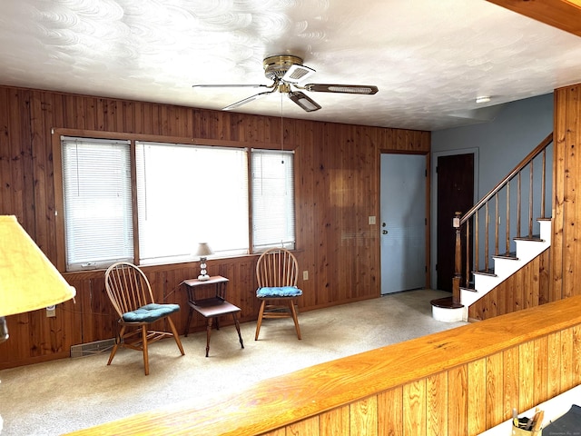 living area featuring wooden walls, carpet flooring, stairs, and a ceiling fan