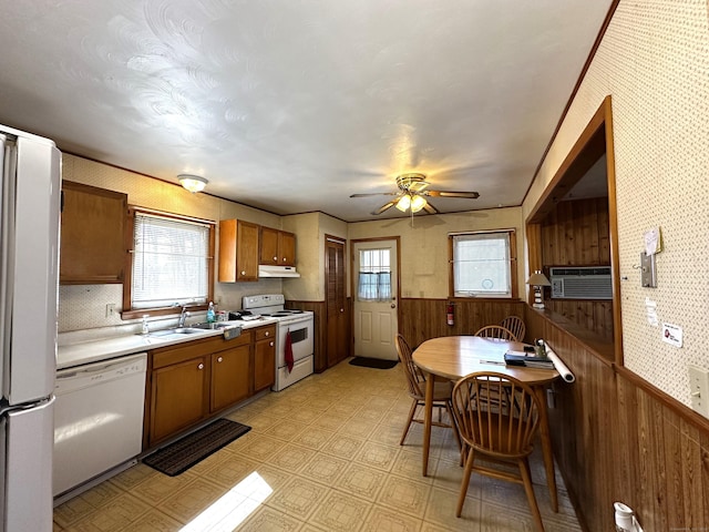 kitchen with a wealth of natural light, a wainscoted wall, white appliances, and brown cabinets