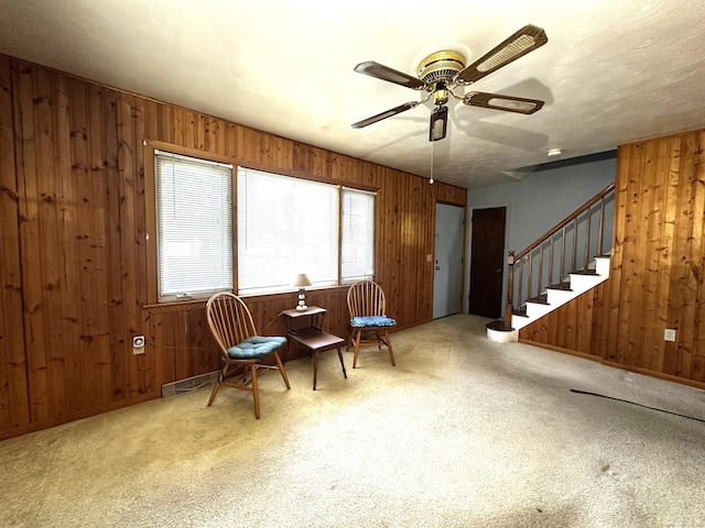 sitting room featuring wooden walls, a ceiling fan, visible vents, and carpet floors