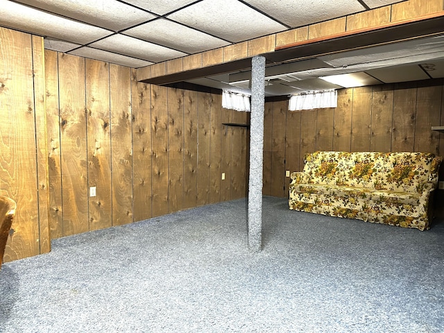 finished basement with a paneled ceiling, wood walls, and carpet floors