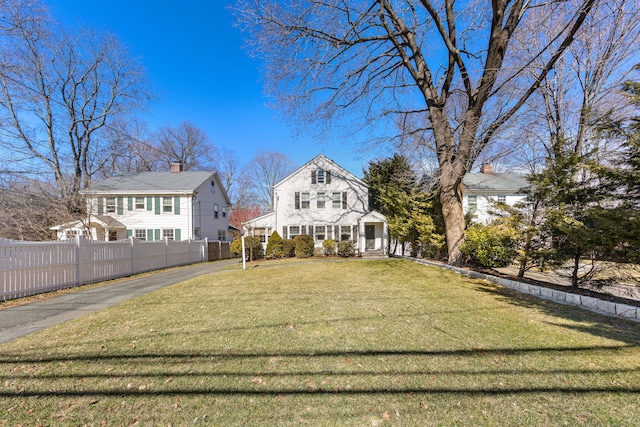 view of front facade with a chimney, a front lawn, and fence