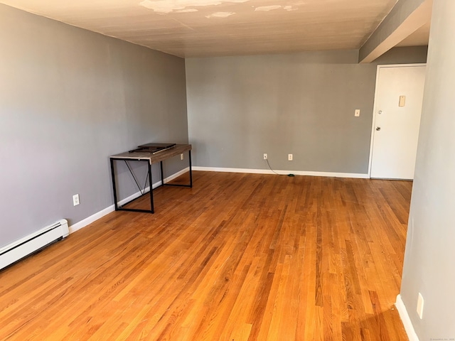 unfurnished room featuring a baseboard heating unit, light wood-style floors, and baseboards