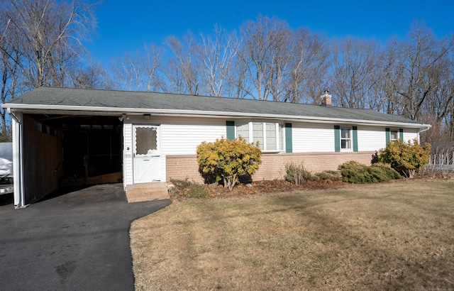 ranch-style home featuring aphalt driveway, brick siding, a chimney, and a front yard