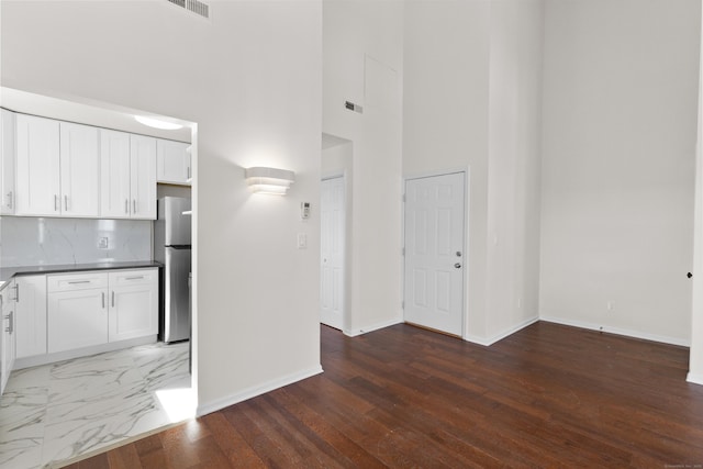 interior space with visible vents, baseboards, wood finished floors, and a towering ceiling