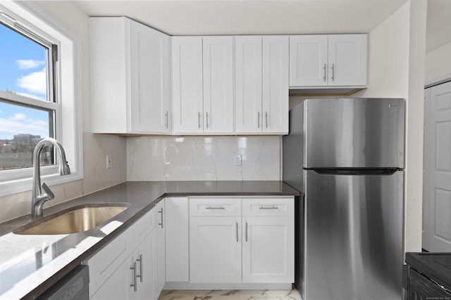 kitchen featuring dark stone countertops, a sink, freestanding refrigerator, white cabinets, and dishwashing machine