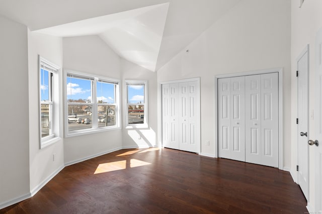 unfurnished bedroom featuring high vaulted ceiling, two closets, baseboards, and wood finished floors