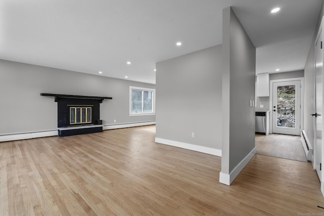 unfurnished living room with light wood-type flooring, a baseboard radiator, plenty of natural light, and a brick fireplace