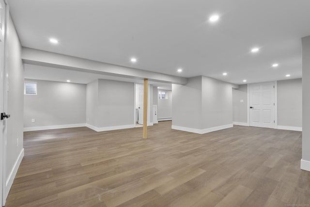 finished below grade area featuring recessed lighting, wood finished floors, baseboards, and a baseboard radiator