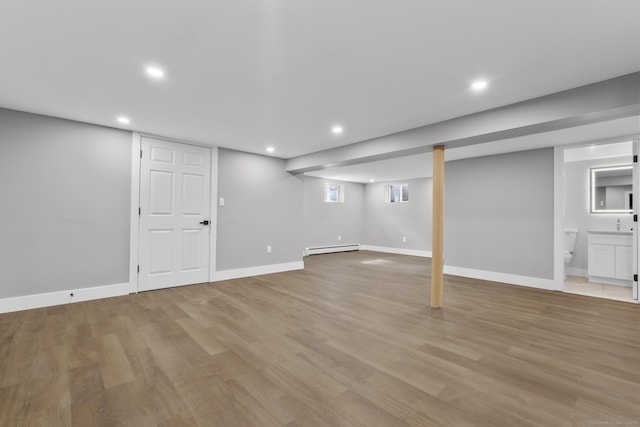 basement featuring light wood-type flooring, a baseboard radiator, baseboards, and recessed lighting