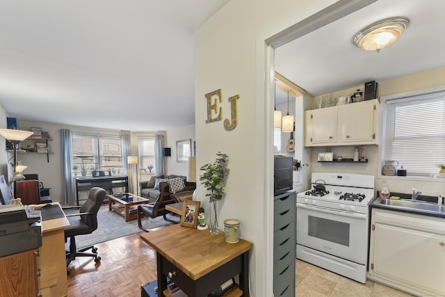 kitchen with tasteful backsplash, open floor plan, white gas range, white cabinetry, and a sink