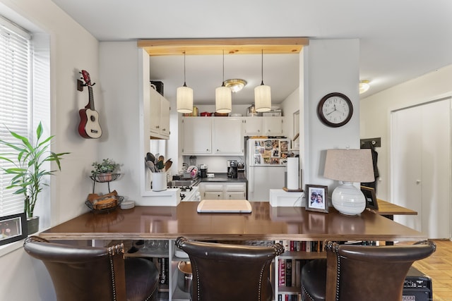 kitchen featuring white cabinetry, dark countertops, hanging light fixtures, and freestanding refrigerator