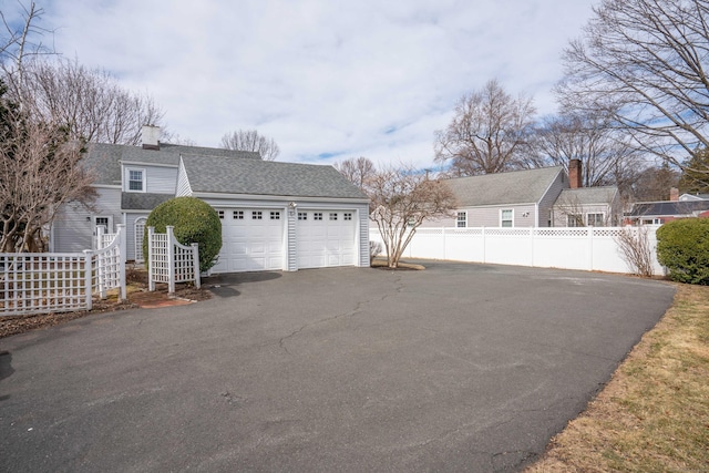 exterior space with a shingled roof, fence, a garage, and a chimney