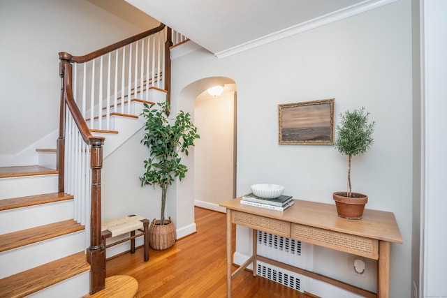 stairs with arched walkways, crown molding, baseboards, and wood finished floors