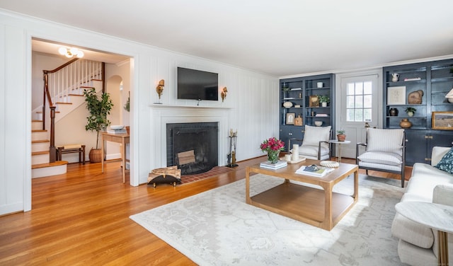 living room featuring wood finished floors, a fireplace with flush hearth, arched walkways, ornamental molding, and stairs