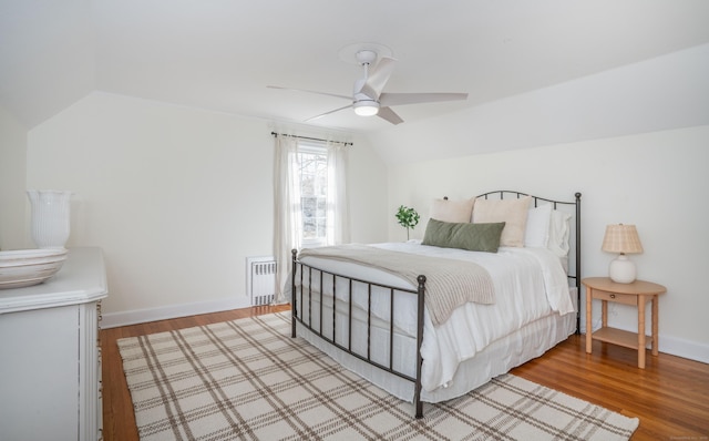 bedroom with a ceiling fan, baseboards, radiator heating unit, vaulted ceiling, and light wood-style floors