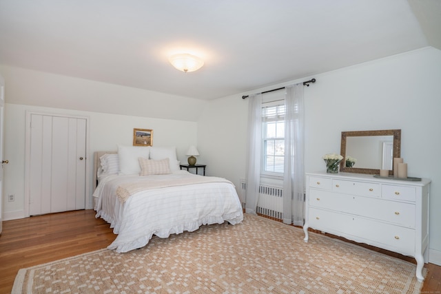 bedroom featuring vaulted ceiling, light wood-style flooring, and radiator