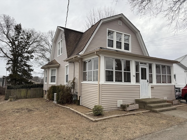 dutch colonial with a gambrel roof, a sunroom, a shingled roof, and fence