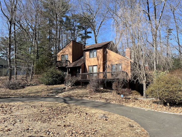 view of front of property with aphalt driveway, a wooden deck, and a chimney