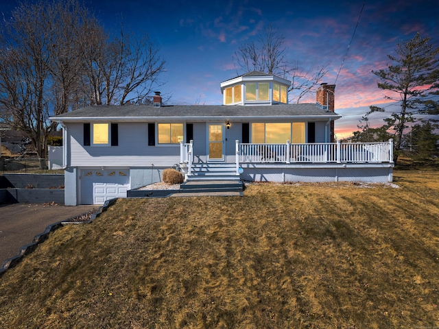 view of front of property featuring driveway, an attached garage, covered porch, a chimney, and a lawn