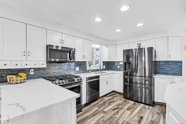 kitchen featuring light stone counters, a sink, white cabinetry, stainless steel appliances, and light wood-style floors