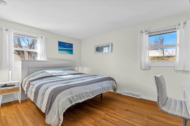 bedroom with visible vents, multiple windows, baseboards, and wood finished floors