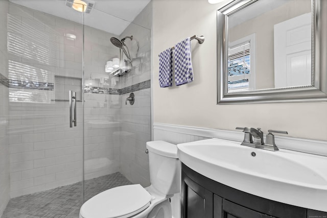 full bathroom featuring a wainscoted wall, a shower stall, toilet, and vanity