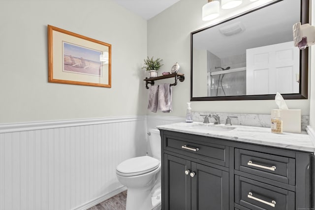 bathroom featuring a wainscoted wall, toilet, wood finished floors, a shower stall, and vanity