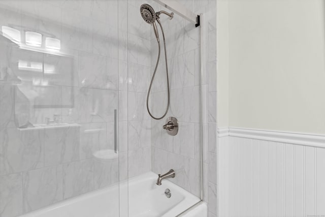 bathroom featuring a wainscoted wall and shower / bath combination with glass door