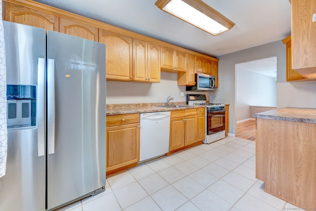 kitchen with baseboards, light countertops, light tile patterned floors, stainless steel appliances, and a sink