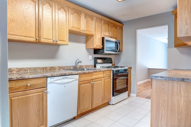 kitchen with a sink, stainless steel microwave, gas range oven, light countertops, and dishwasher