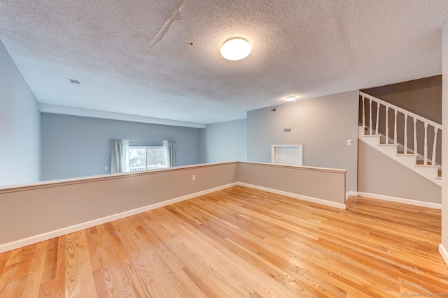 unfurnished room featuring a textured ceiling, stairs, baseboards, and wood finished floors