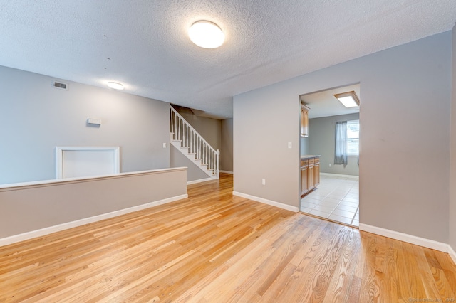 unfurnished room with stairway, visible vents, baseboards, a textured ceiling, and light wood-type flooring